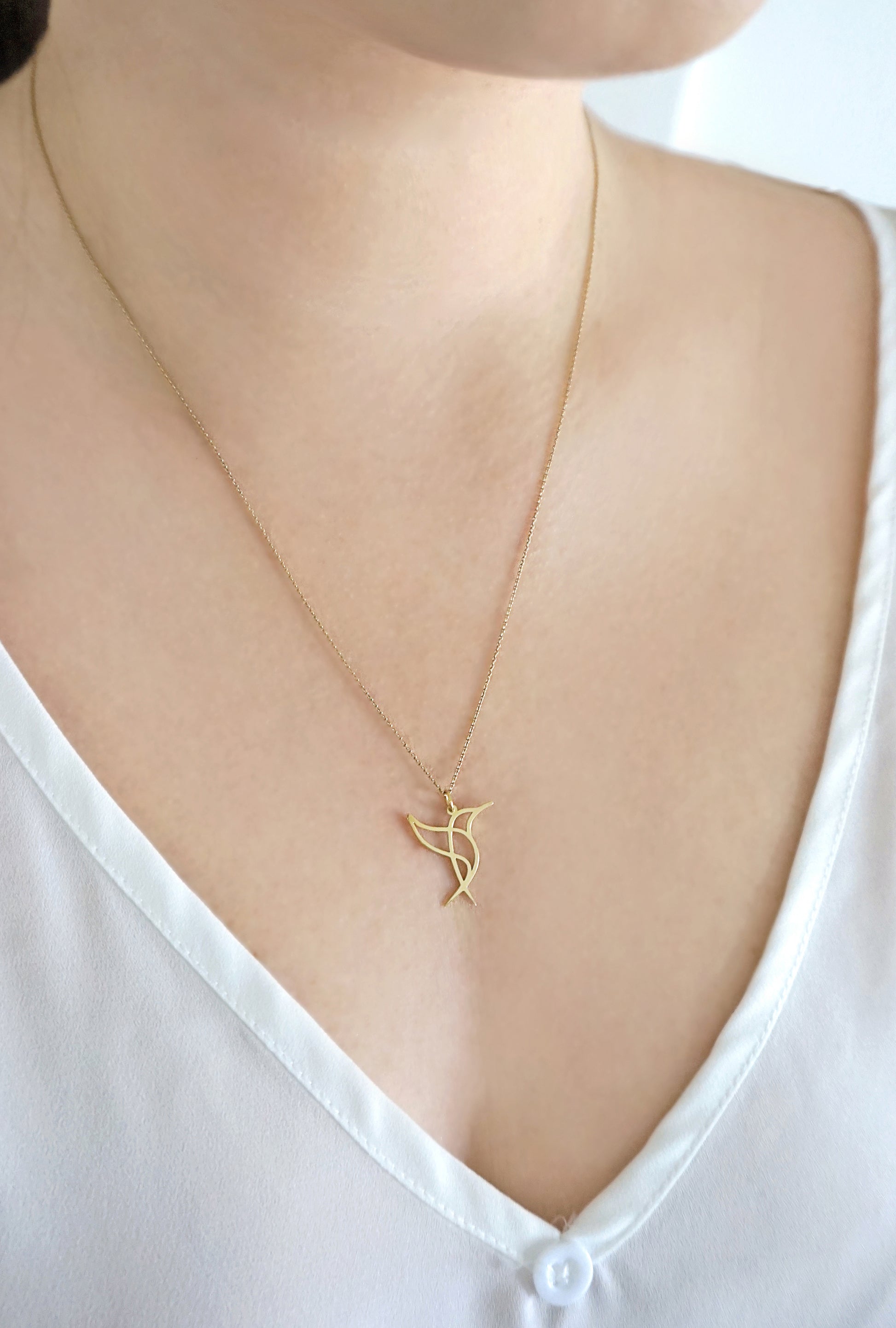 close up of a woman's neck wearing a long gold necklace with a cutout pendant in the shape of a hummingbird