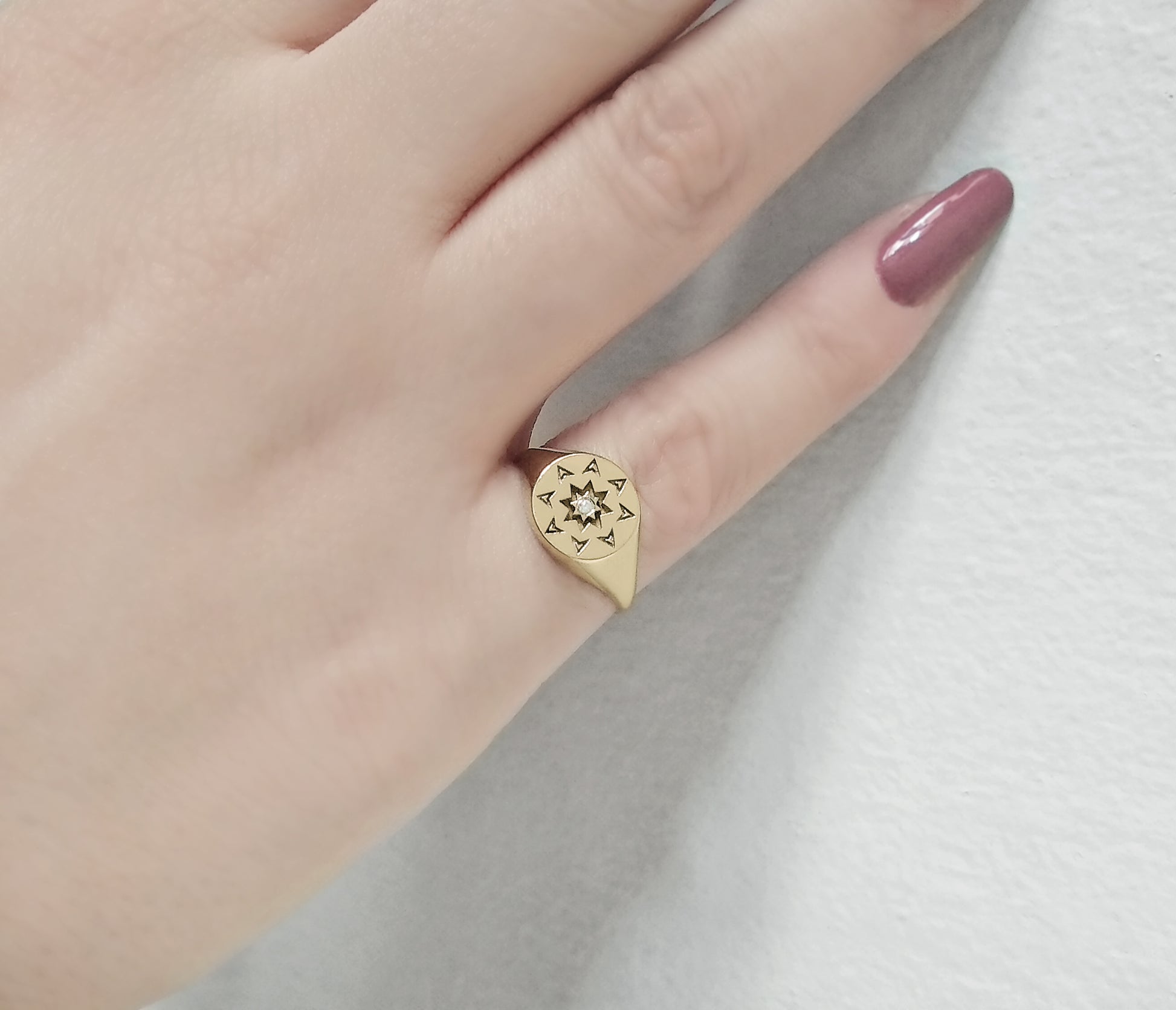 woman's hand wearing a solid yellow gold round signet ring with a north star starburst design and a diamond on the center