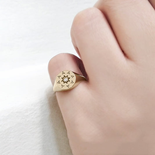 woman wearing on her pinky a solid yellow gold round signet ring with a north star starburst design and a diamond on the center