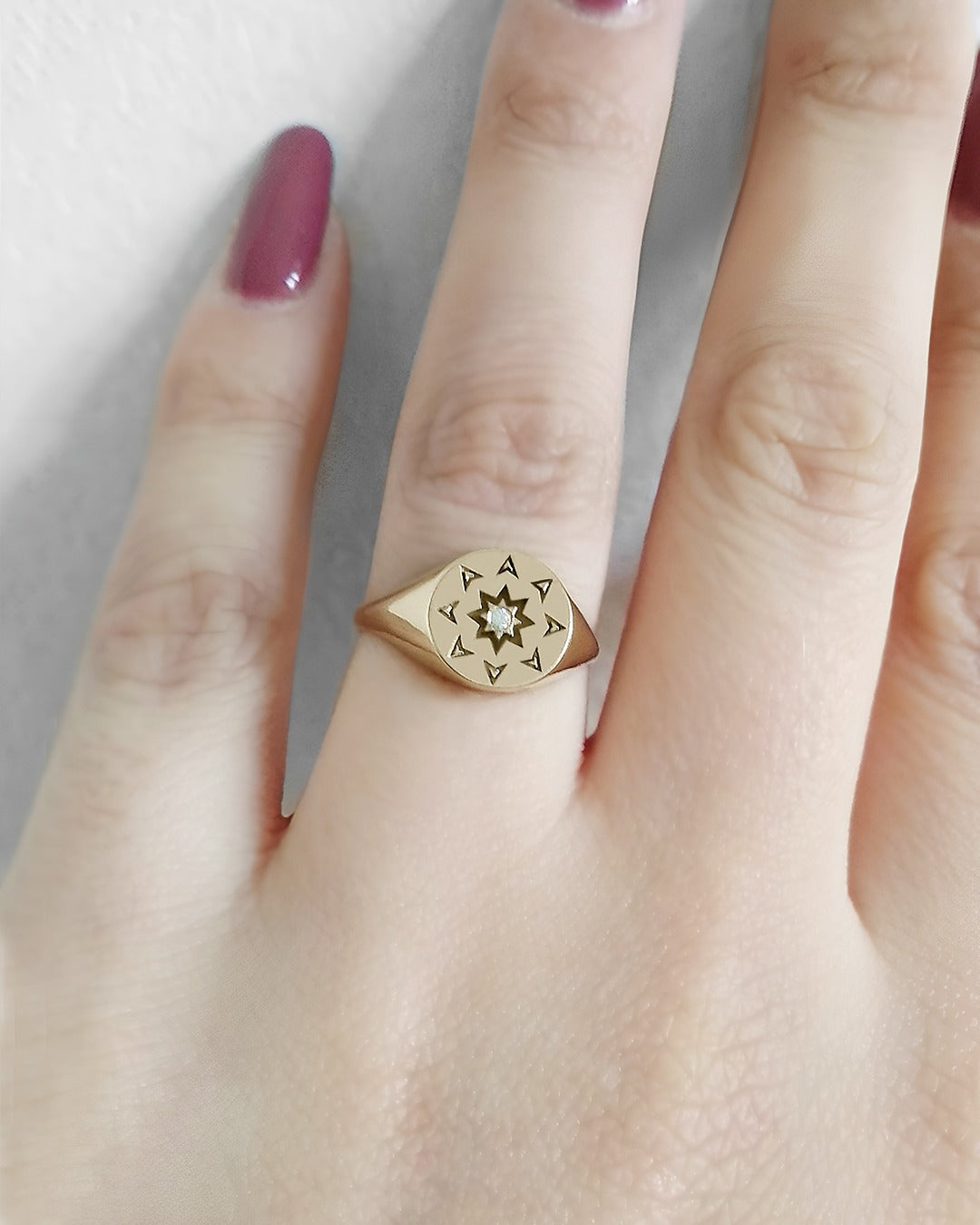 female wearing on her ring finger a solid yellow gold round signet ring with a north star starburst design and a diamond on the center