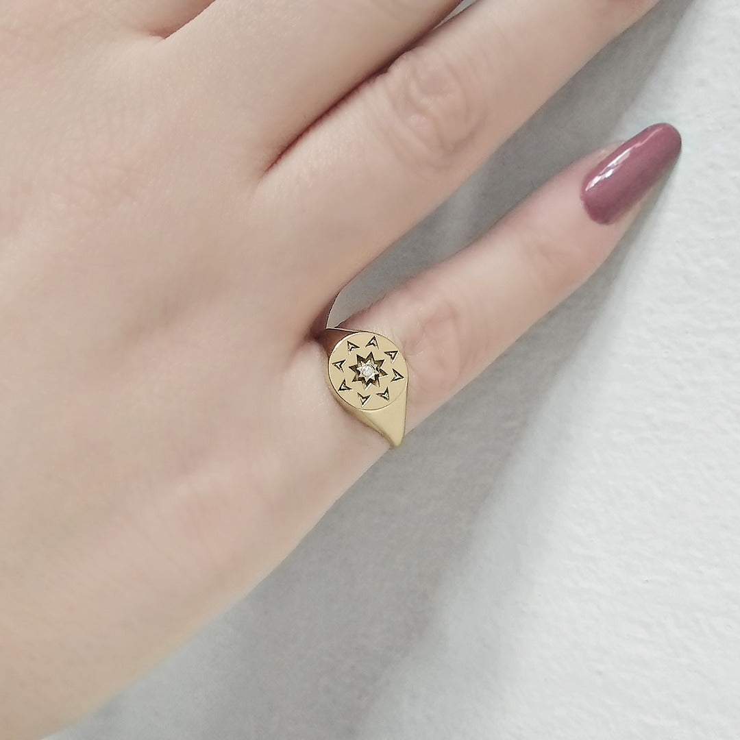 woman's hand wearing a solid yellow gold round signet ring with a north star starburst design and a diamond on the center