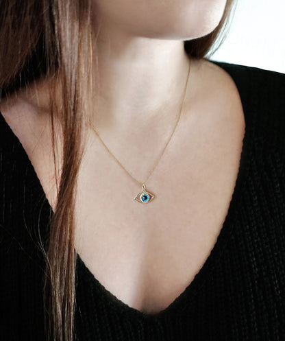 Gold necklace with an eye-shaped pendant with diamonds worn by a person against a neutral background