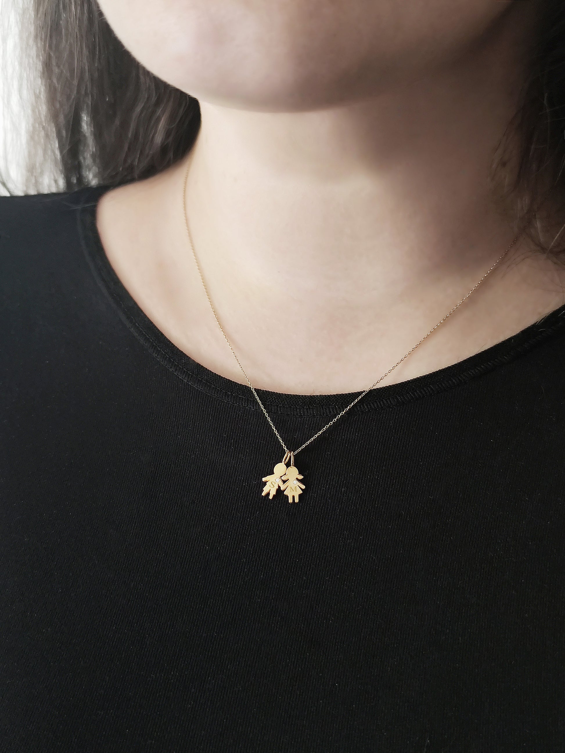 close up of a woman's neck wearing a gold necklace with a tiny boy and a tiny girl charm engraved with monograms and set with tiny diamond