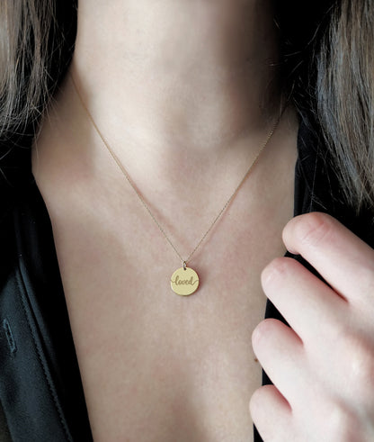 Gold necklace with a pendant engraved with the word 'loved' on a woman's neck