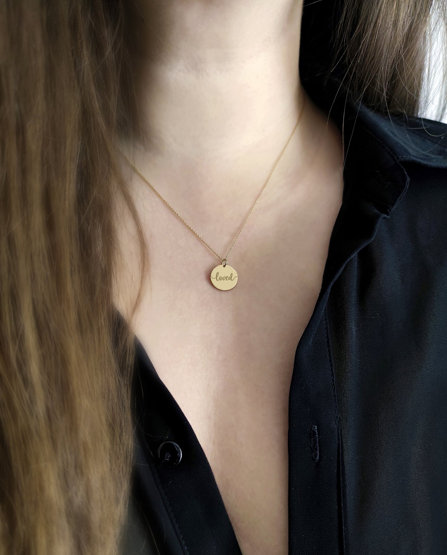 Gold necklace with a round pendant engraved with the word 'loved' worn by a female.