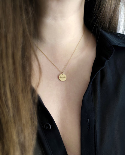 Gold necklace with a round pendant engraved with the word 'loved' worn by a female.