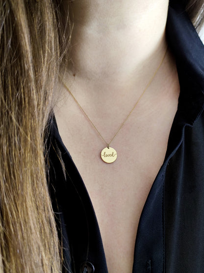 Gold necklace with a 'loved' pendant worn by a female