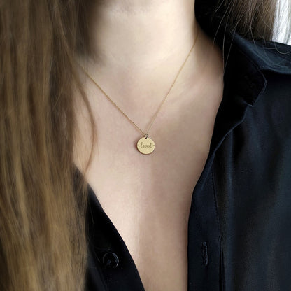 Gold necklace with a disc pendant engraved with the word 'loved' worn by a female