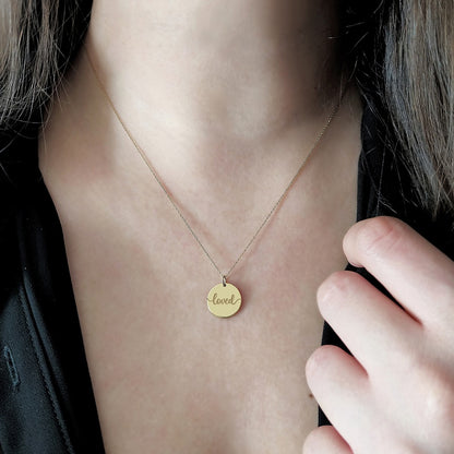 Gold necklace with a 'loved' pendant on a person's neck