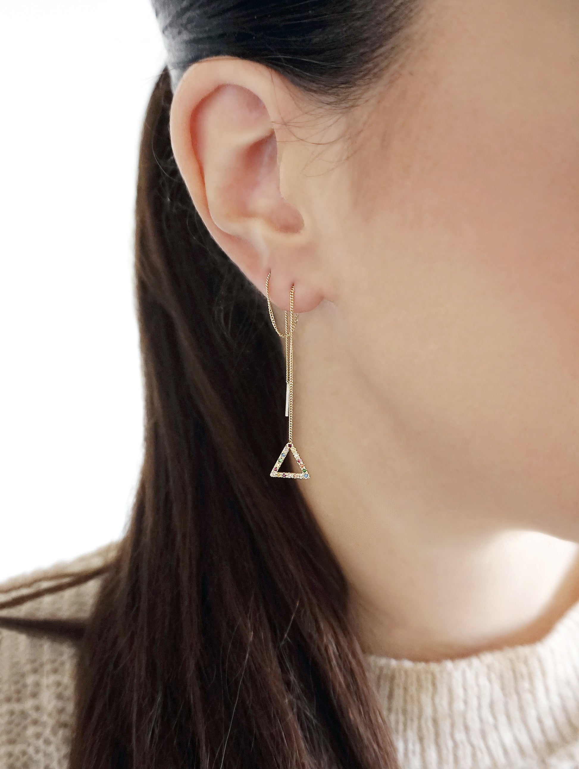 female wearing a threader earring pulled through two piercings with a small triangle at the end set with rainbow sapphires and made in solid yellow gold