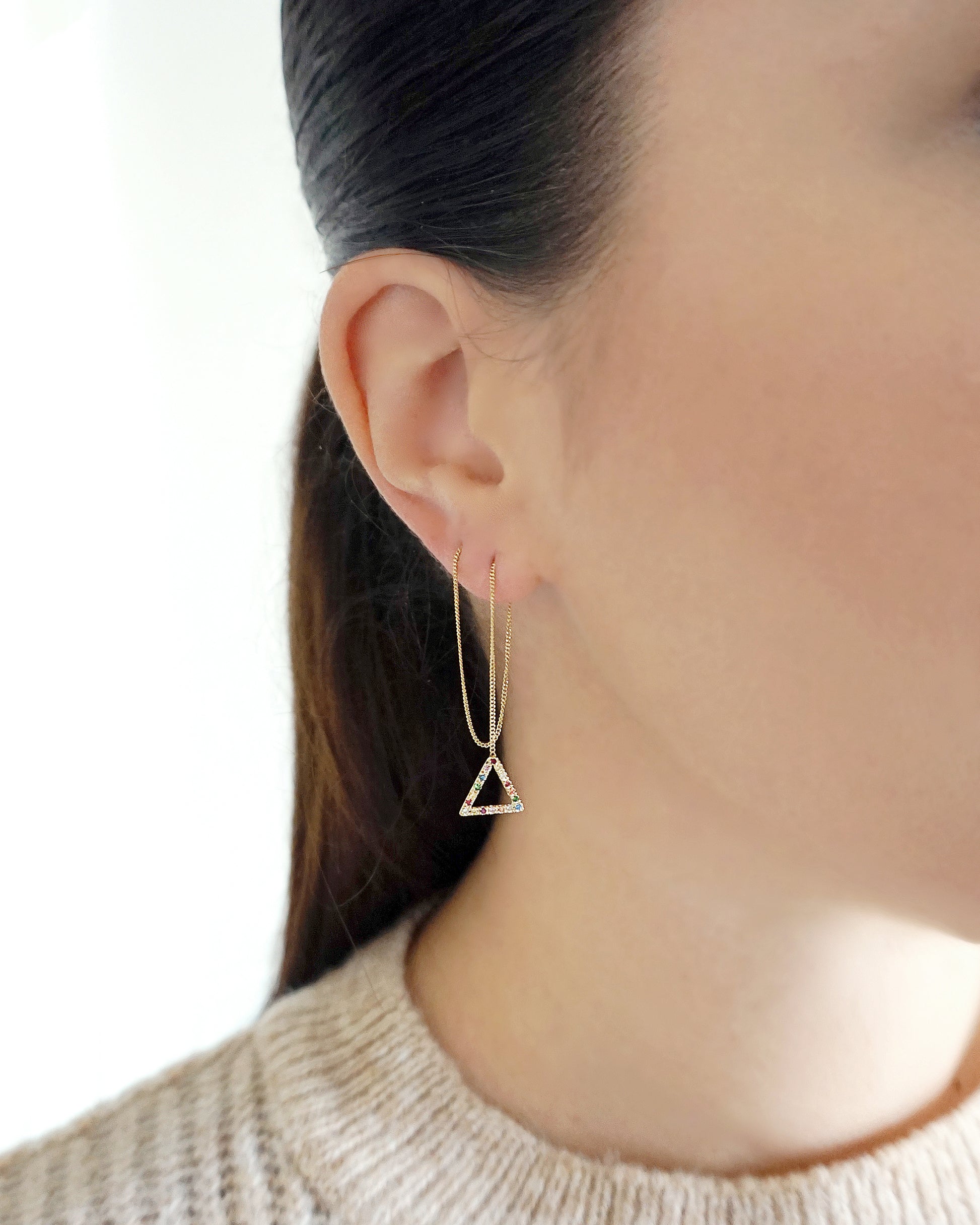 woman wearing a threader earring pulled through two piercings with a small triangle at the end set with rainbow sapphires and made in solid yellow gold