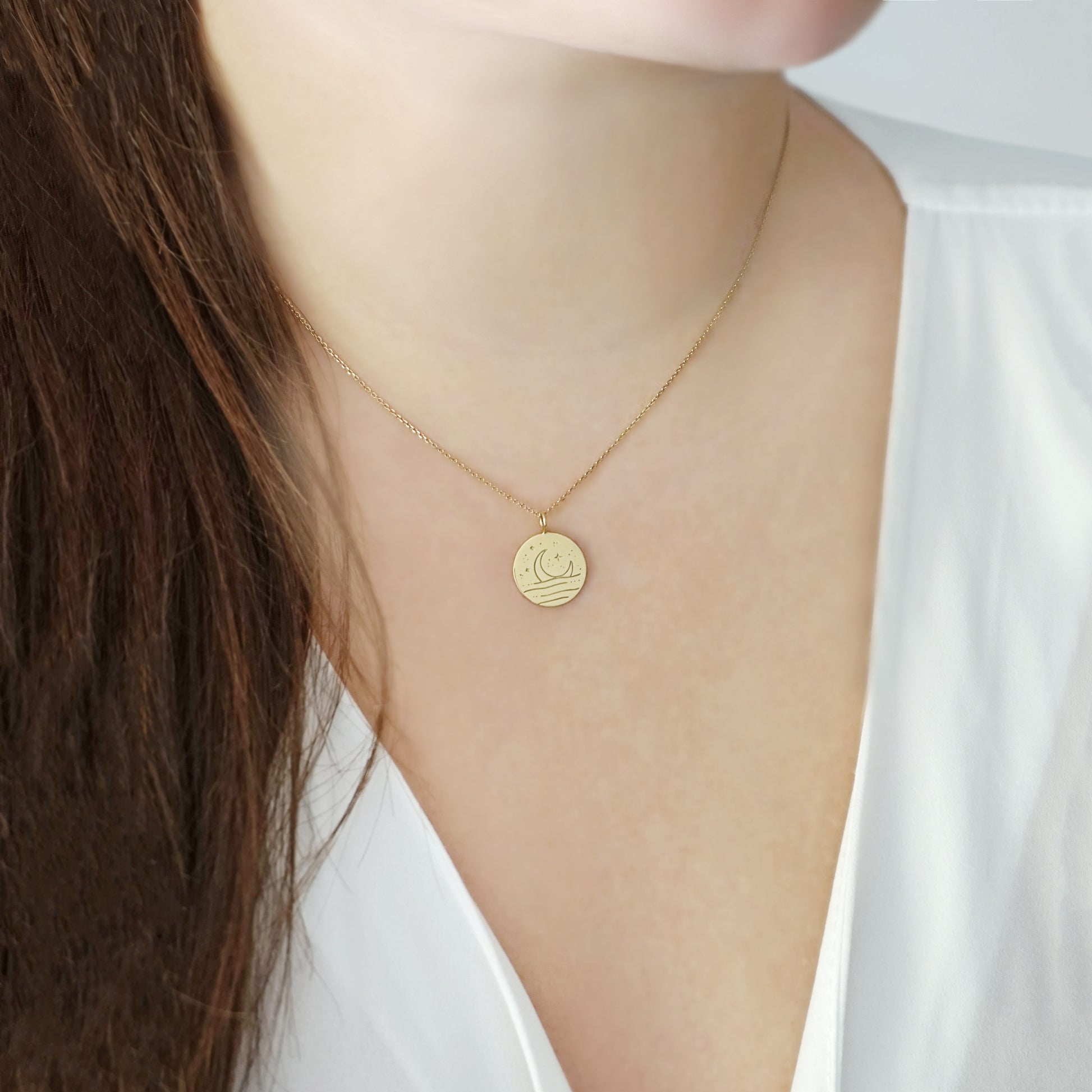 female wearing gold necklace with reversible pendant engraved with a moon on one side and a sun on the other side 