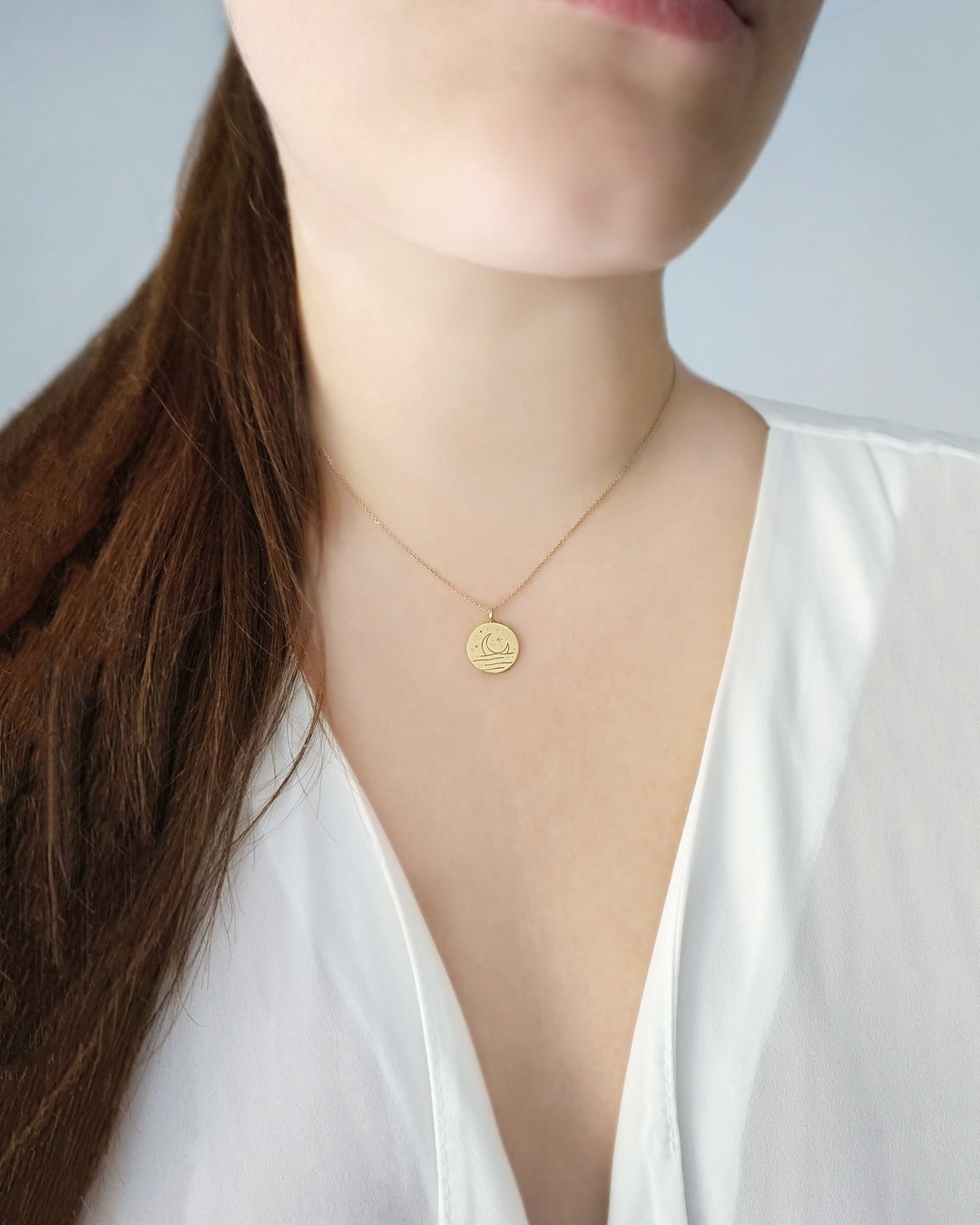 person wearing gold necklace with reversible pendant engraved with a moon on one side and a sun on the other side 