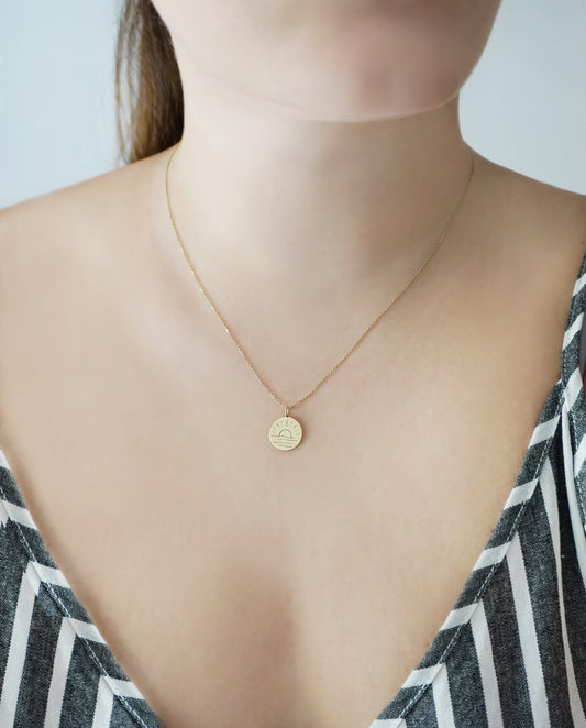 person wearing a gold necklace with reversible pendant engraved with a moon on one side and a sun on the other side 