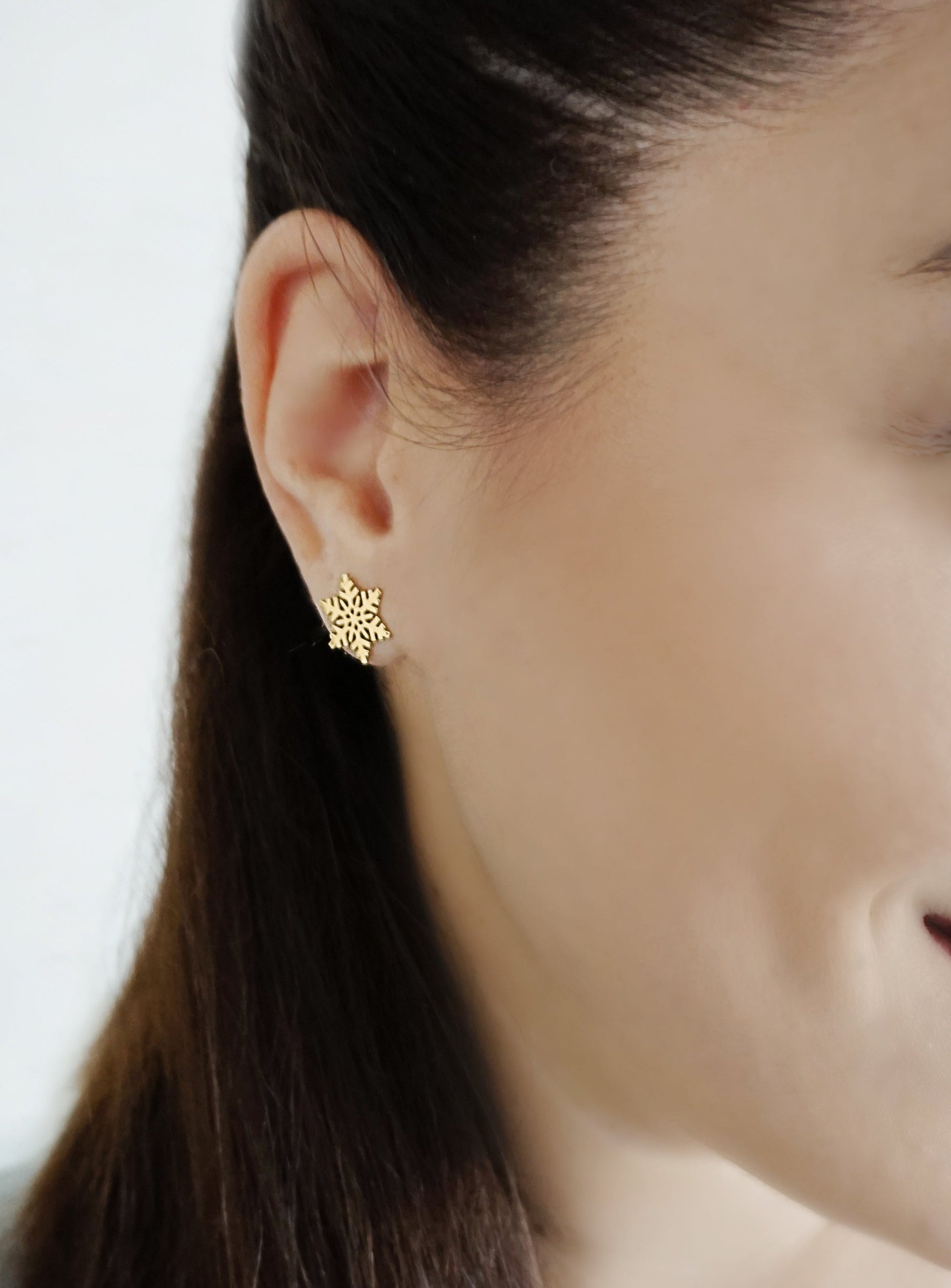close up of a woman's ear wearing yellow gold stud earring in the shape of a snowflake