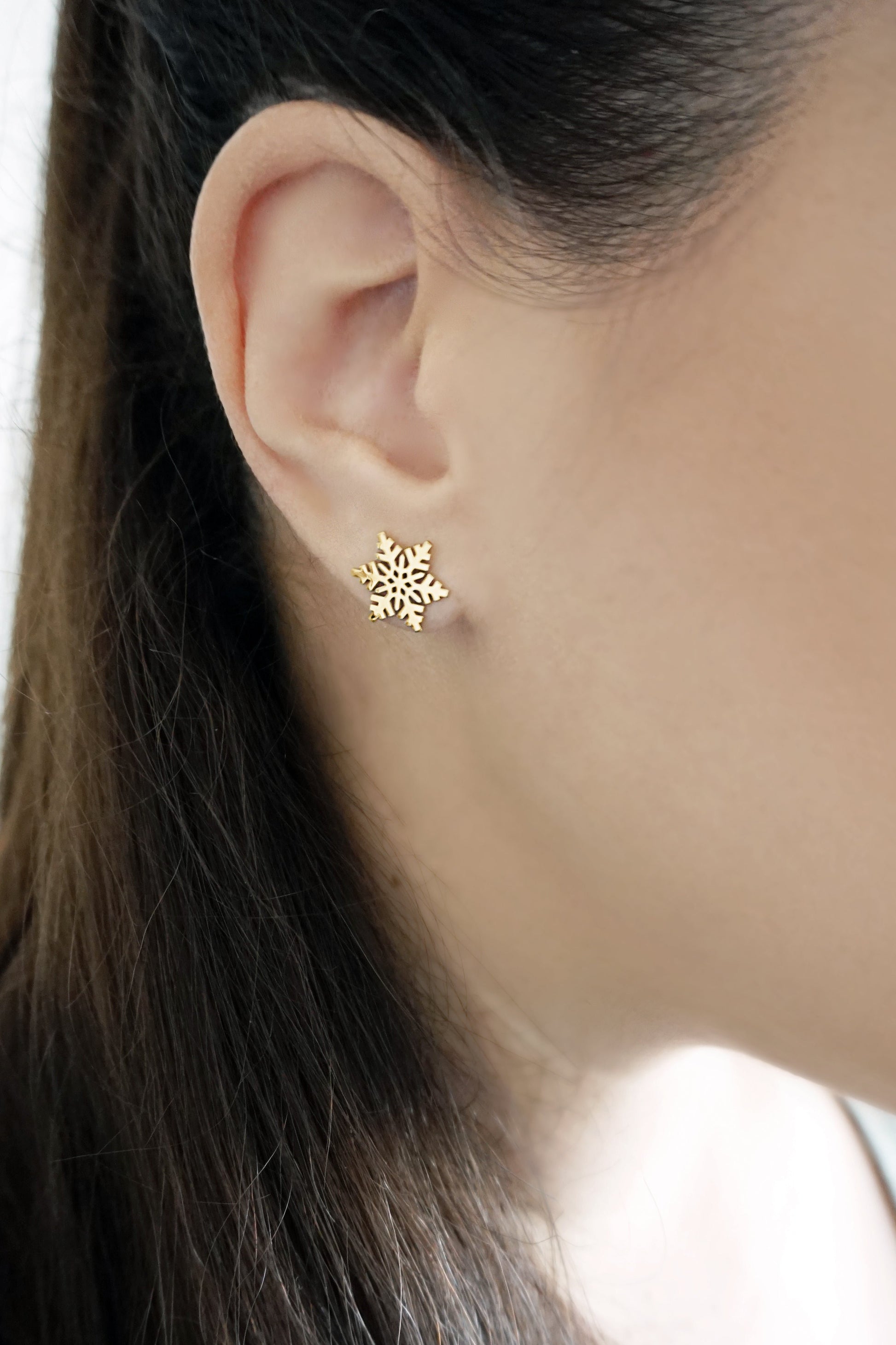 female wearing yellow gold stud earring in the shape of a snowflake