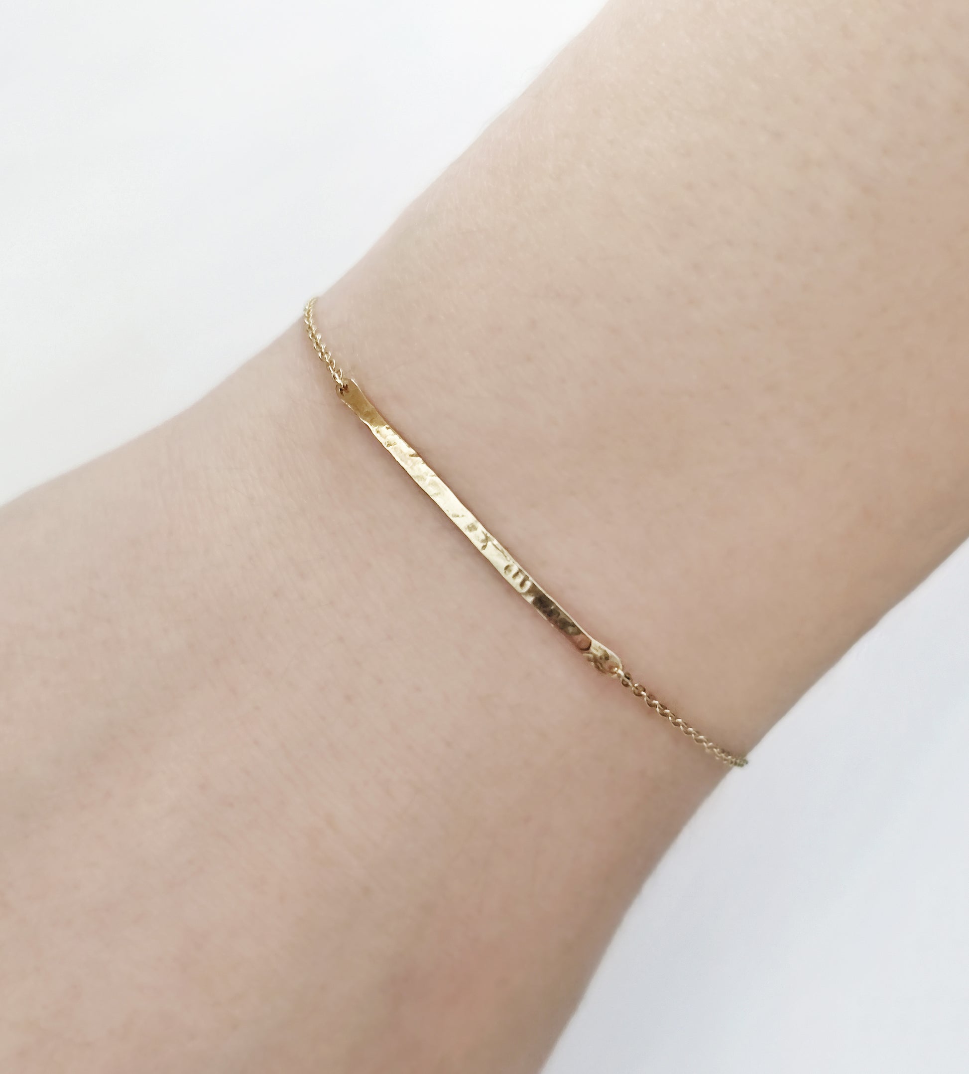woman's wrist wearing a solid yellow gold thin hammered bar bracelet