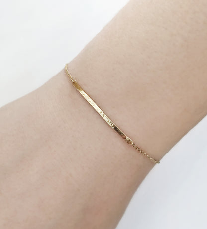 woman's wrist wearing a solid yellow gold thin hammered bar bracelet