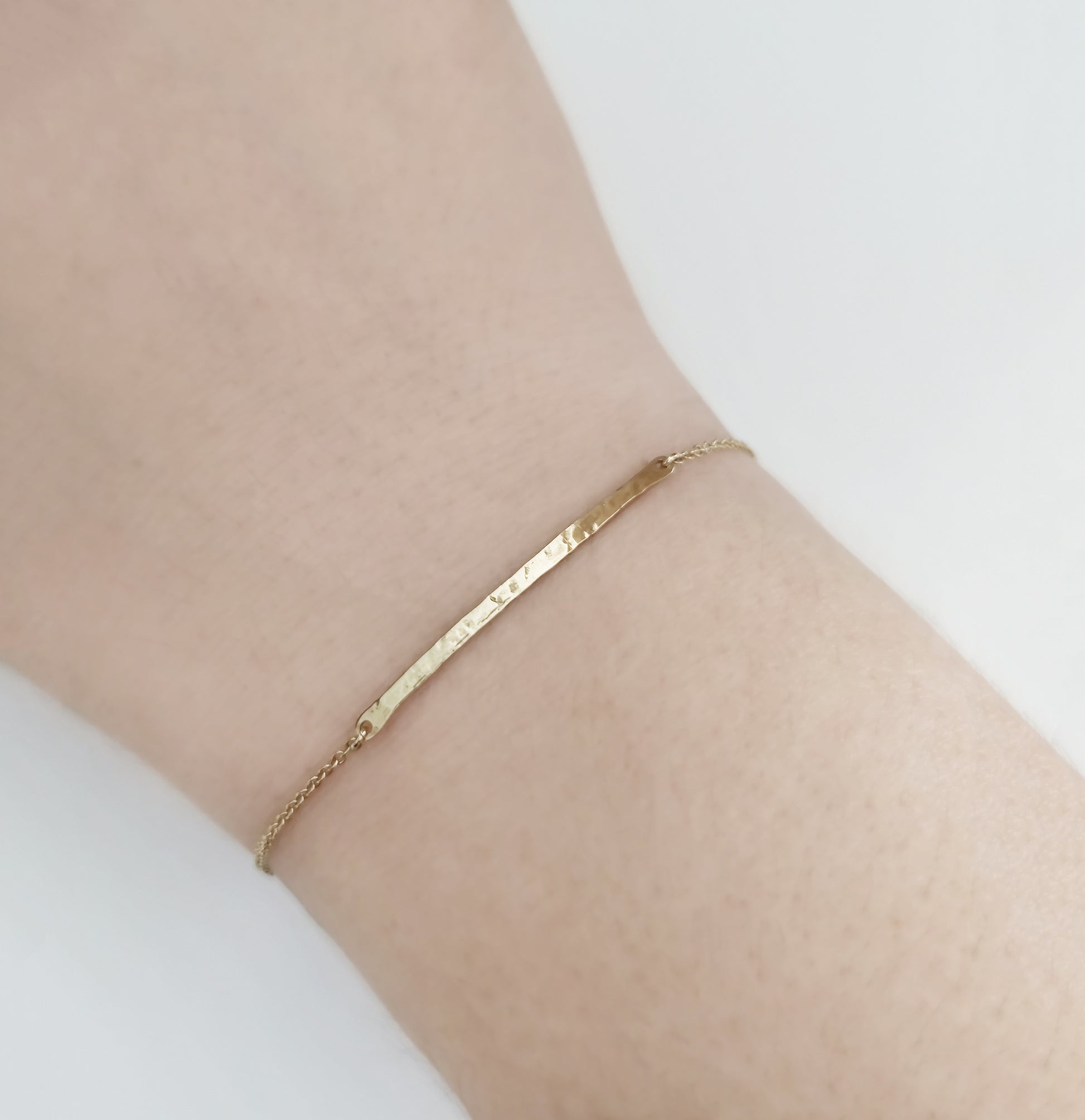 female wrist wearing a gold thin hammered bar bracelet