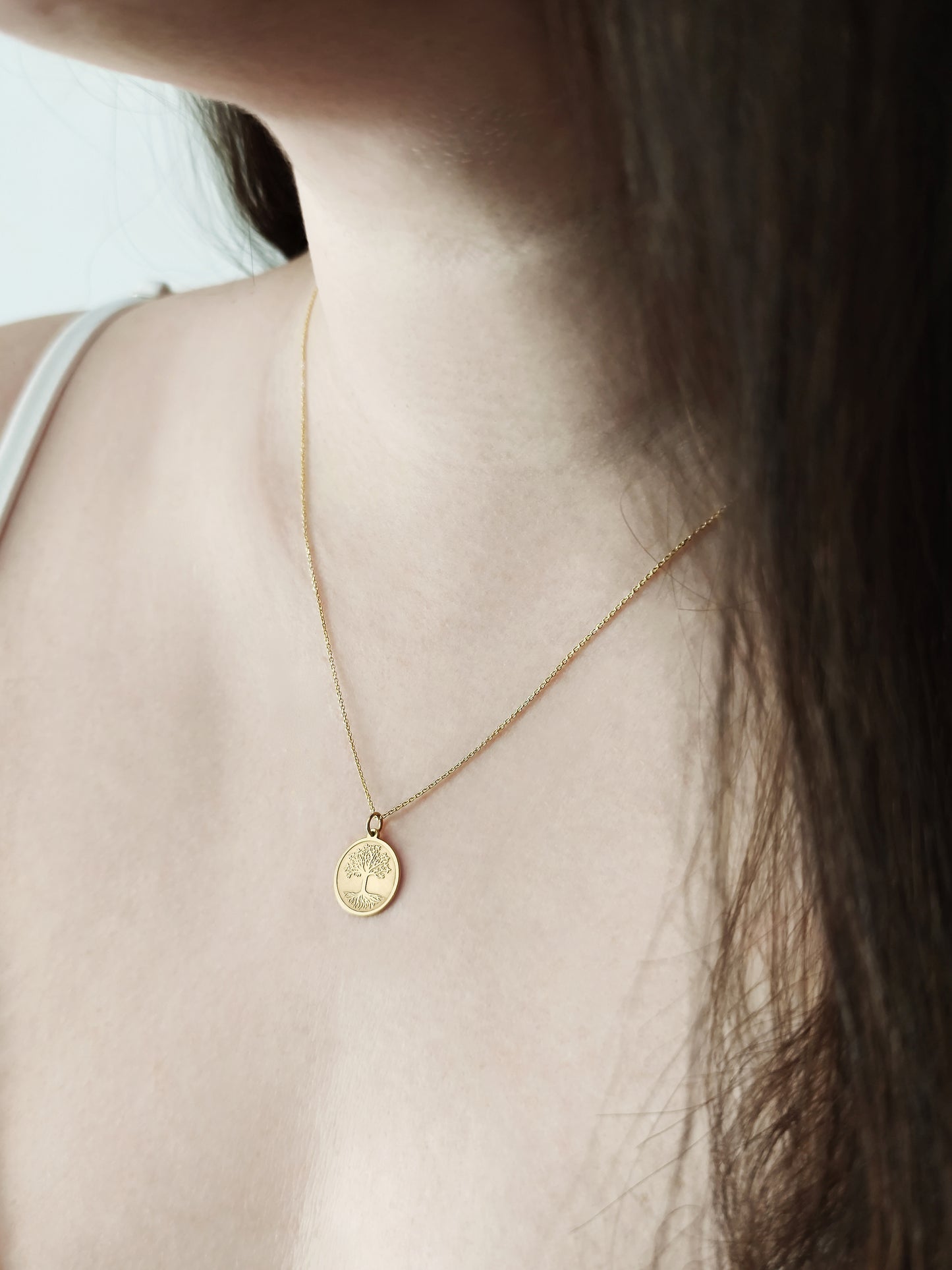 female wearing a yellow gold necklace with a disc pendant engraved with the Tree of Life