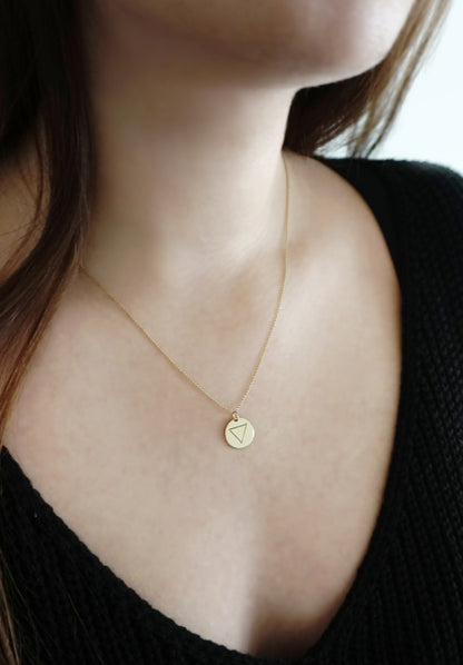 woman wearing a yellow gold necklace with a 14mm disc pendant engraved with the water element symbol