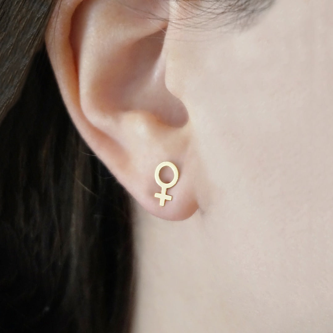 female wearing small gold female/Venus symbol stud earrings