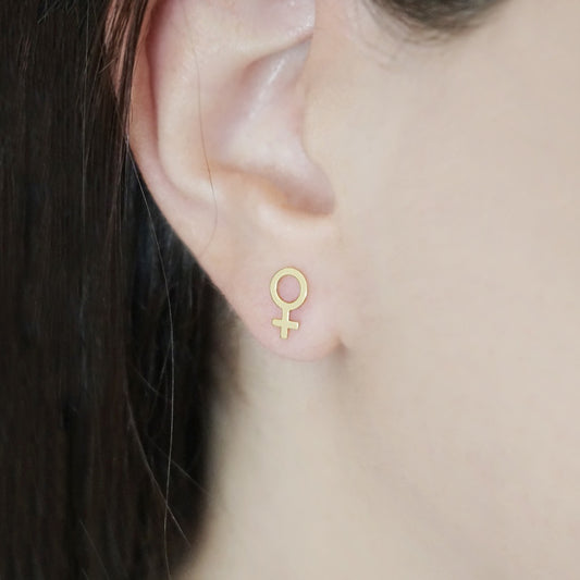 female wearing small solid yellow gold female/Venus symbol stud earrings