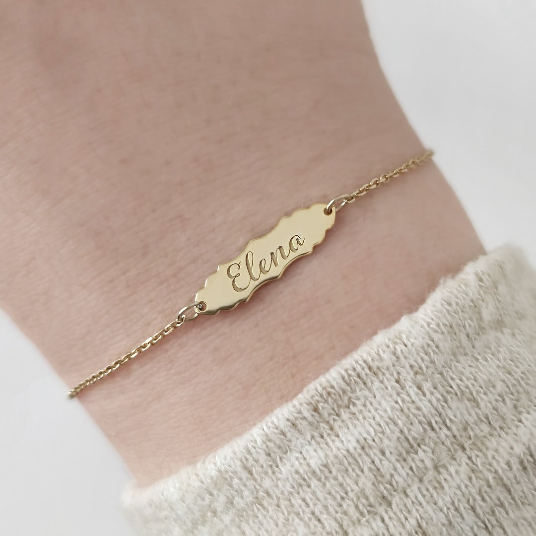 woman's wrist wearing a gold bracelet with a vintage baroque inspired bar engraved with a name