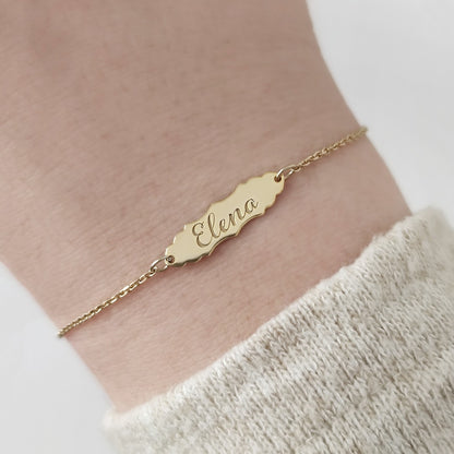 woman's wrist wearing a gold bracelet with a vintage baroque inspired bar engraved with a name