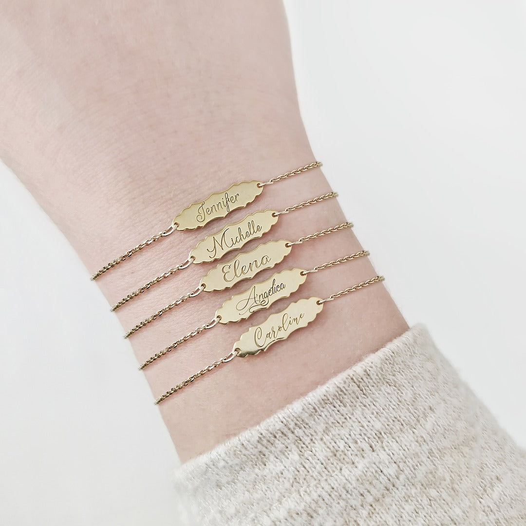 woman wearing gold bracelets with a vintage baroque inspired bar engraved with names written with 5 different fonts