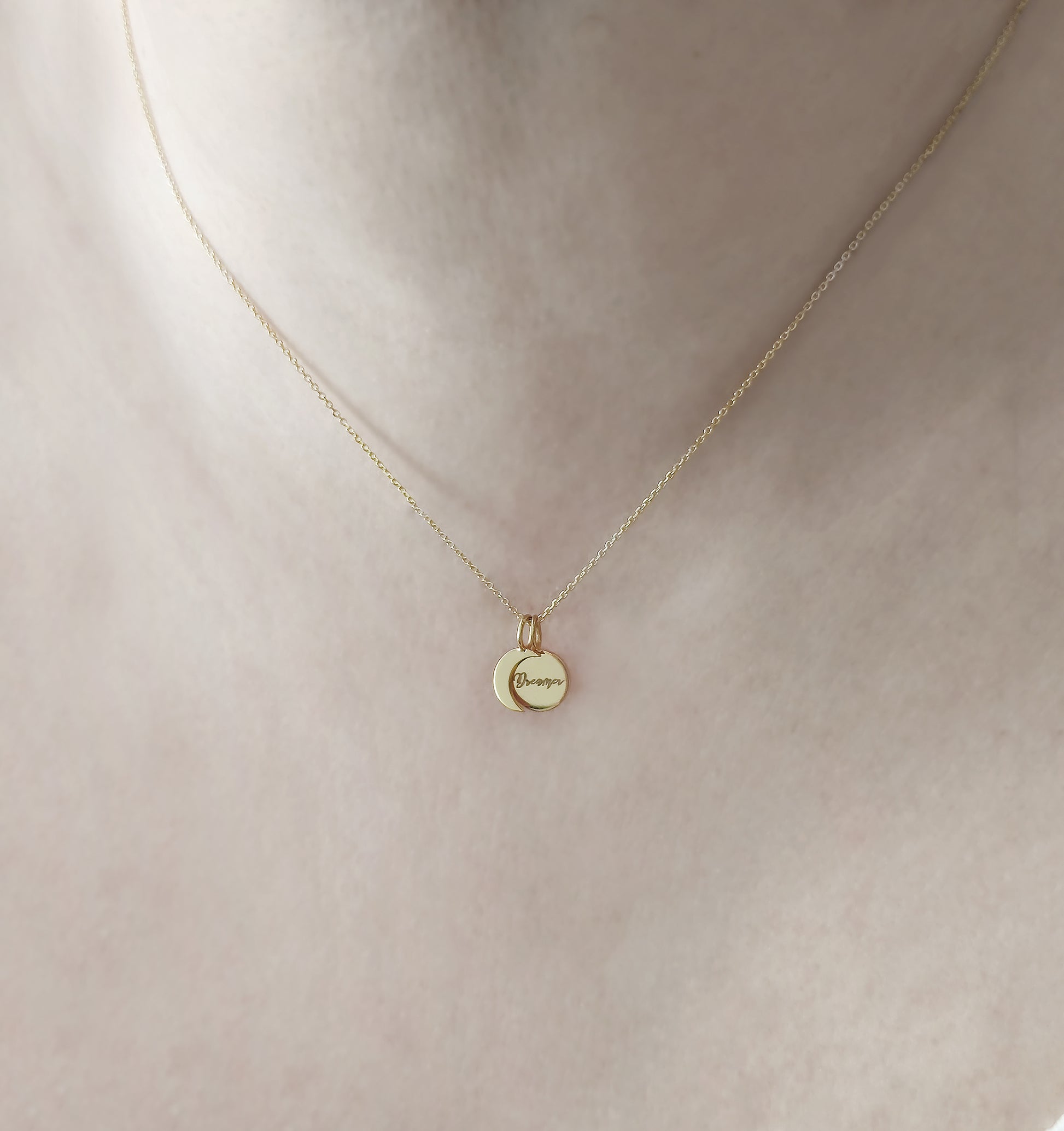 woman's neck wearing gold necklace with two small charms, a crescent moon and a personalized disc