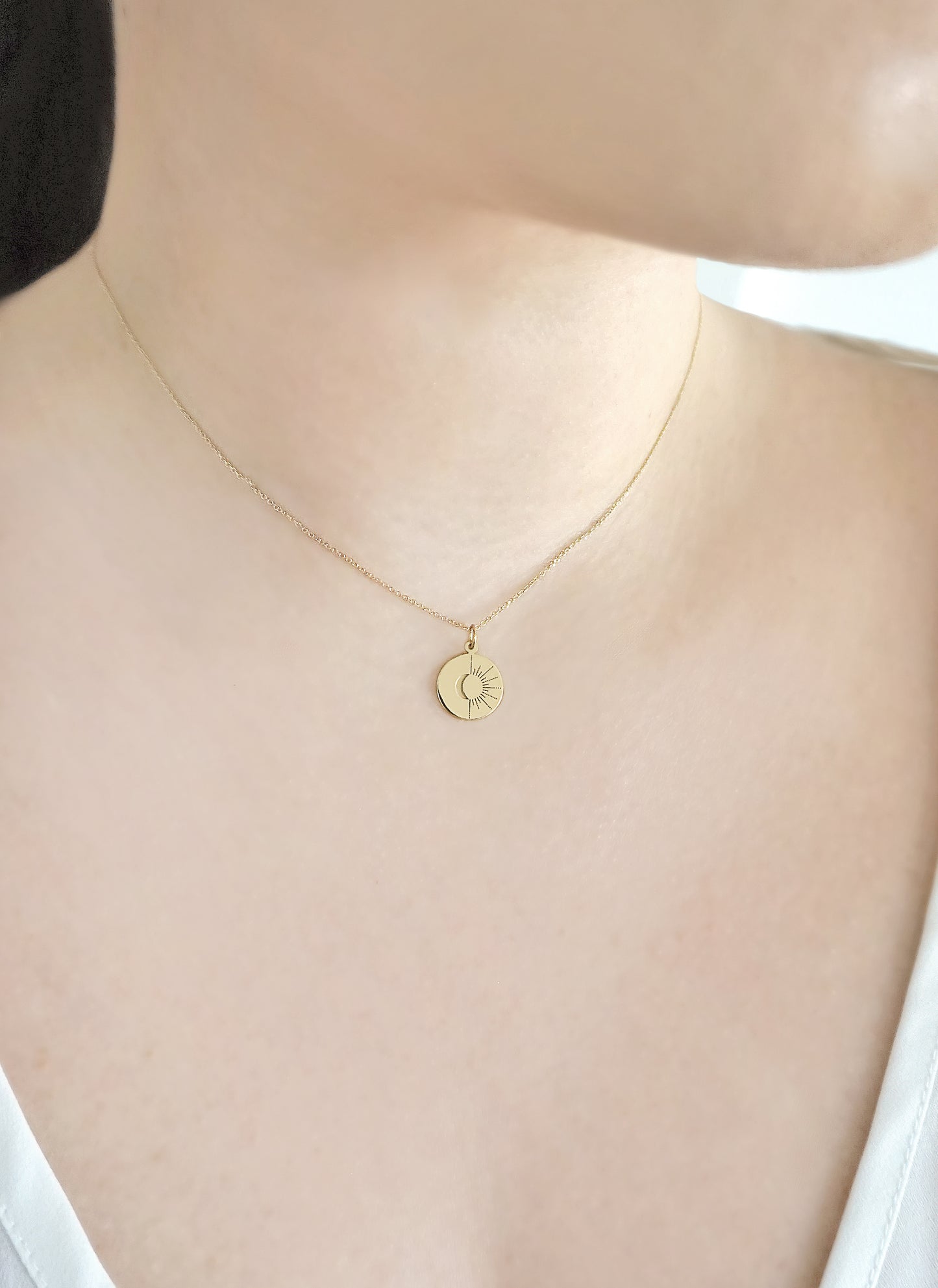 close up of a woman's neck wearing solid gold disc pendant necklace engraved with a sun and moon design