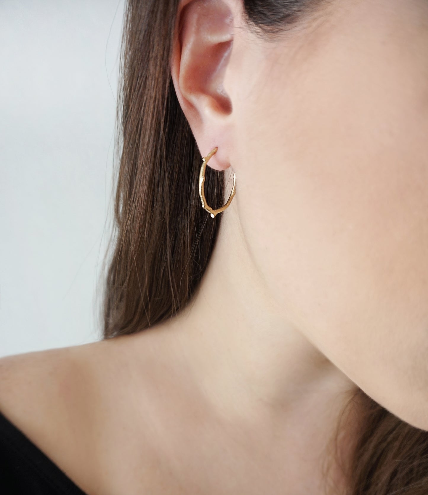 female wearing gold open hoop earring with a twig branch like design and brushed polished finish