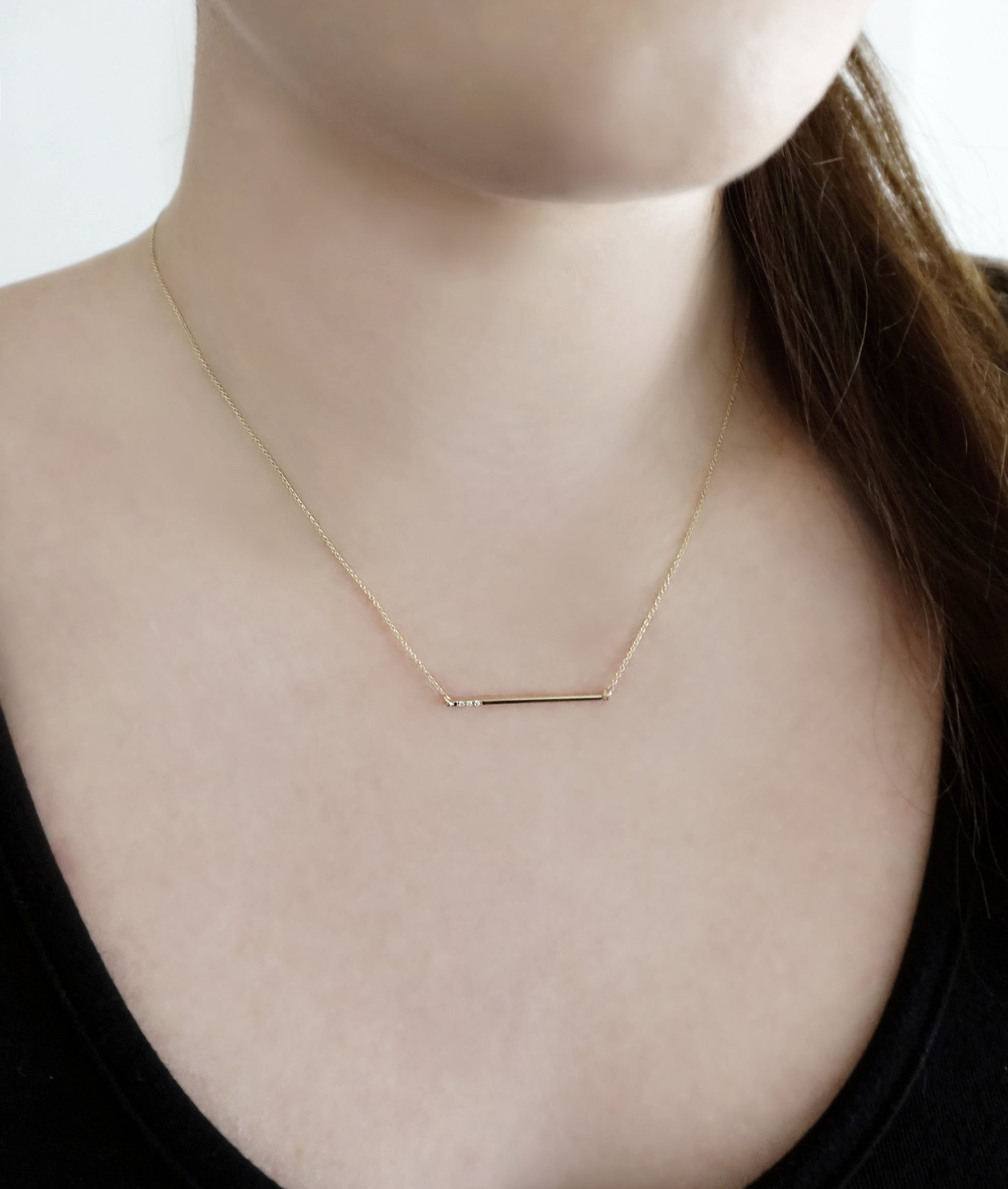 female wearing a solid gold thin bar necklace set with three tiny white diamonds