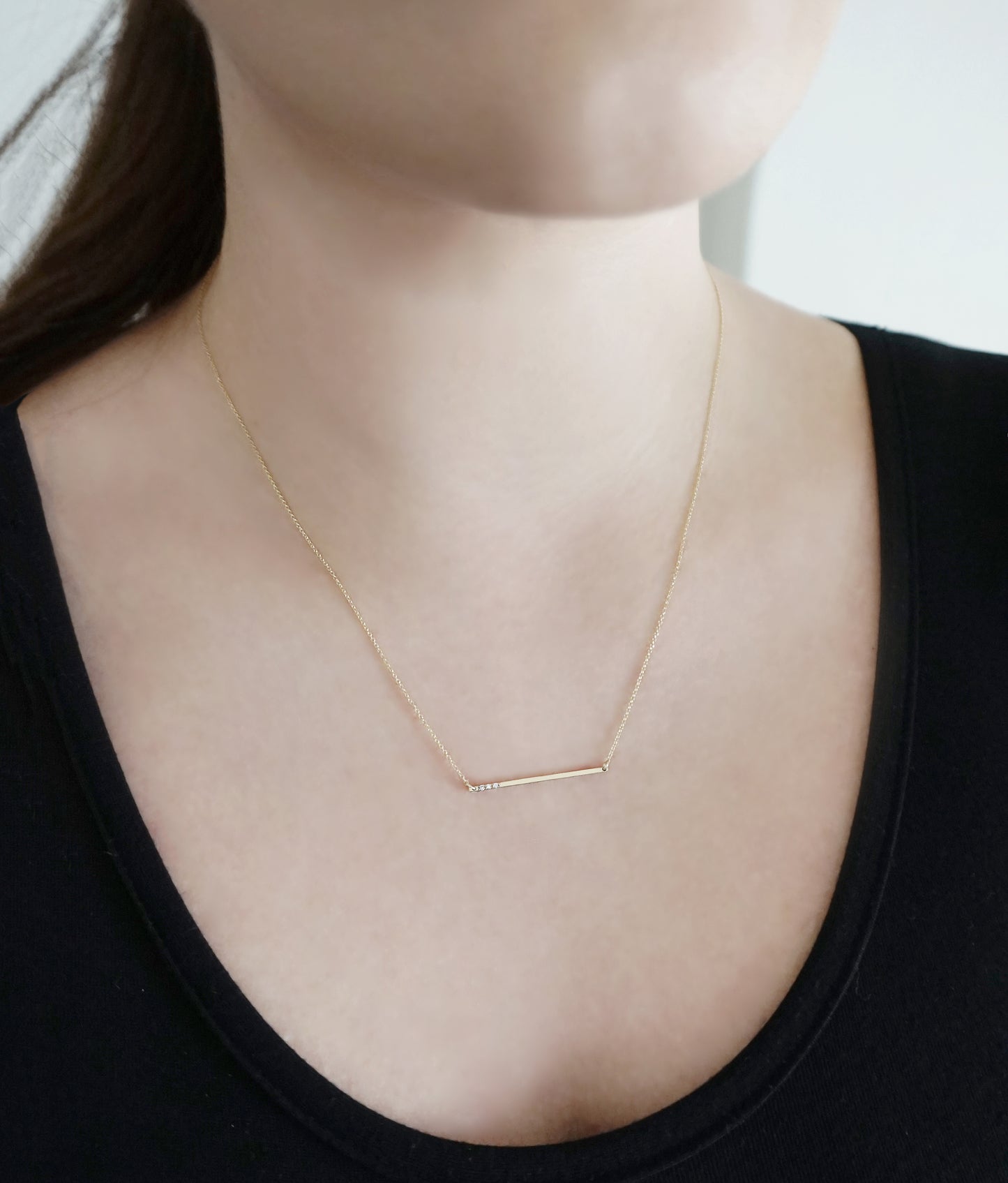 woman wearing 14K gold thin bar necklace set with three tiny white diamonds