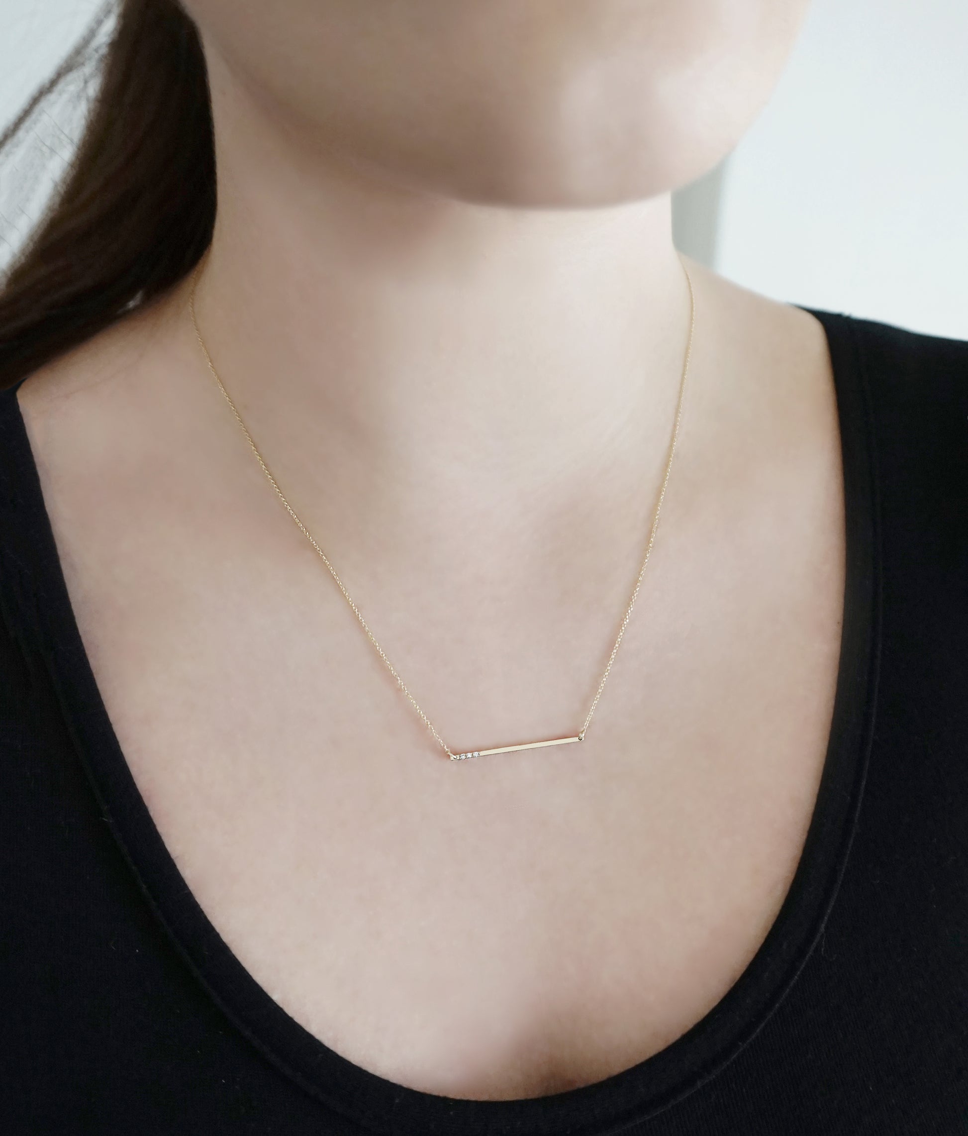 woman wearing 14K gold thin bar necklace set with three tiny white diamonds
