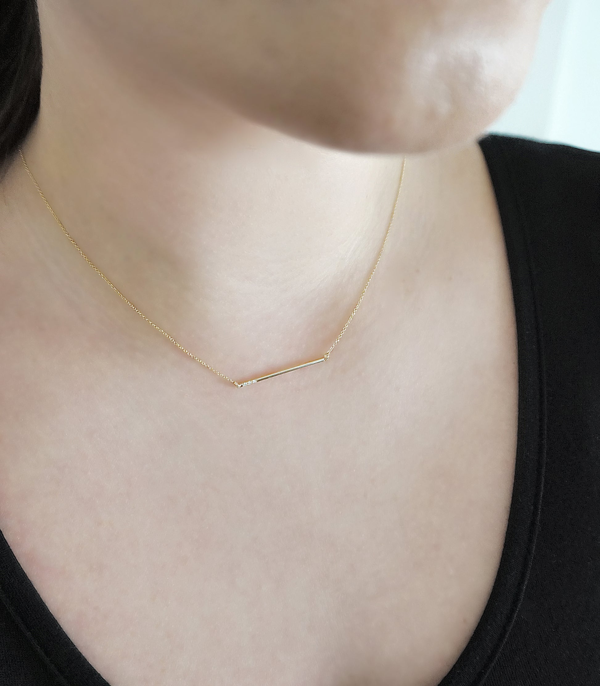 female wearing 14K gold thin bar necklace set with three tiny white diamonds
