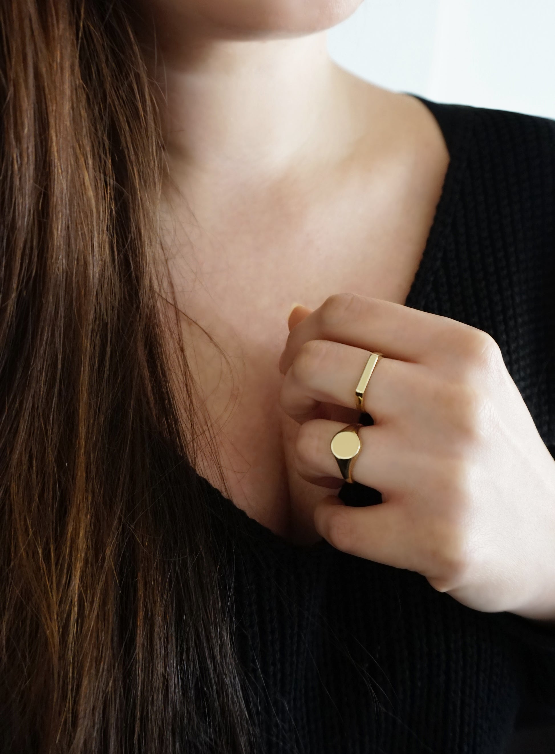 female wearing thin bar ring on her middle finger and a round signet ring on her ring finger