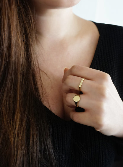 female wearing thin bar ring on her middle finger and a round signet ring on her ring finger