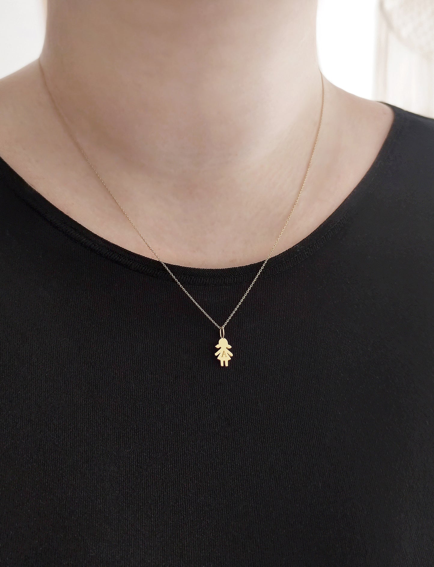 close up of a woman's neck wearing a gold necklace with a tiny girl outline charm engraved with a monogram