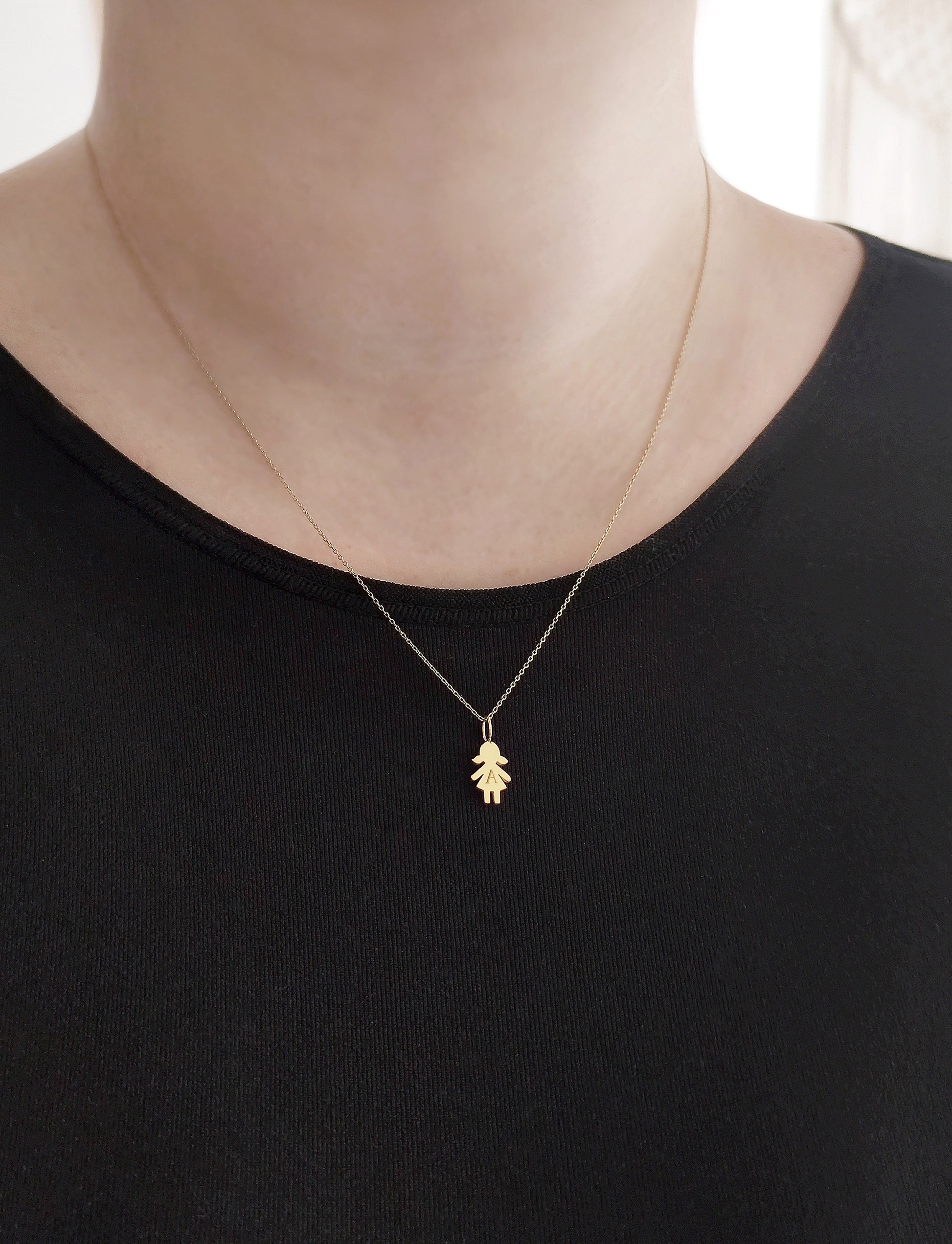 close up of a woman's neck wearing a gold necklace with a tiny girl outline charm engraved with a monogram