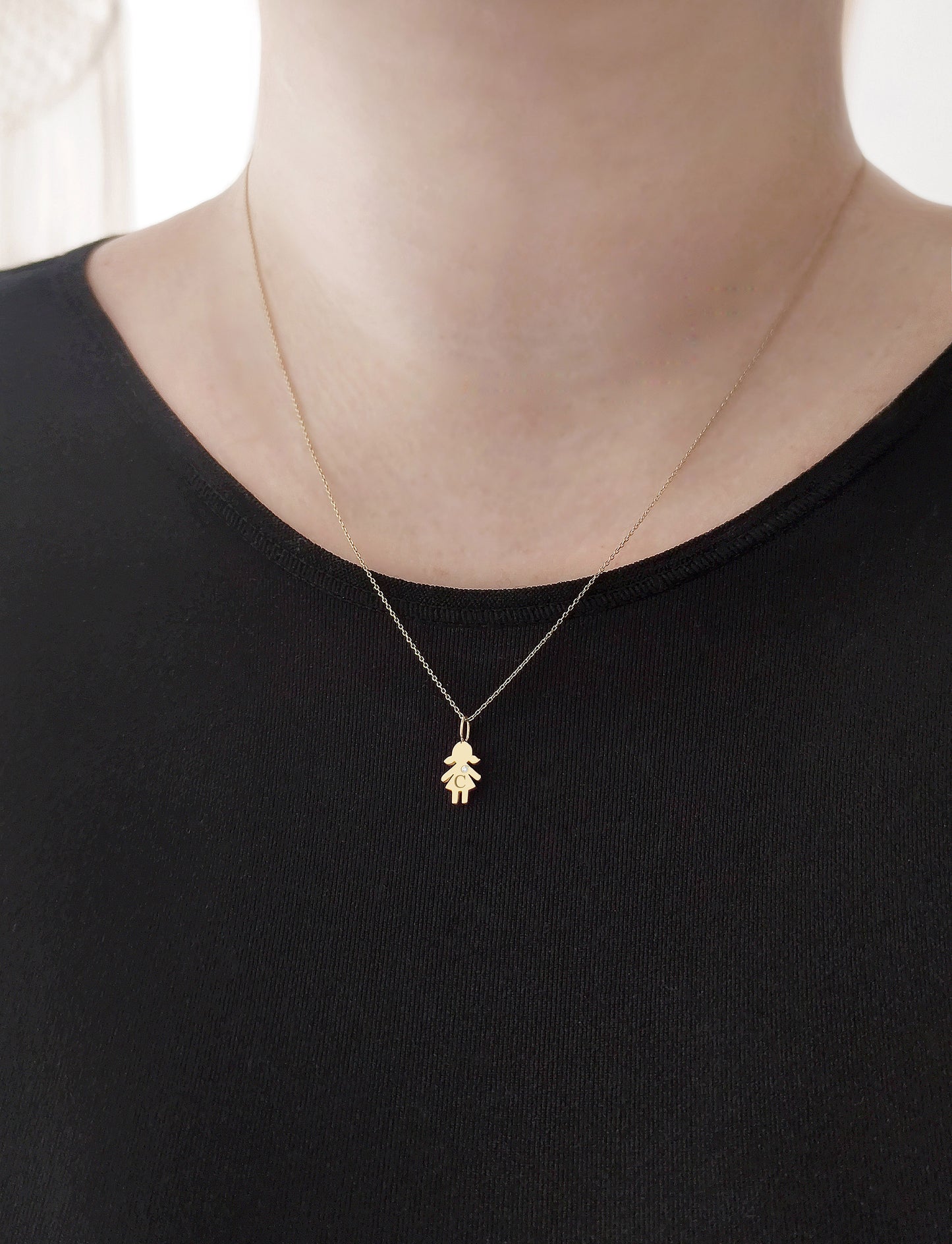 close up of a woman's neck wearing a gold necklace with a tiny girl charm engraved with a monogram and set with a tiny diamond