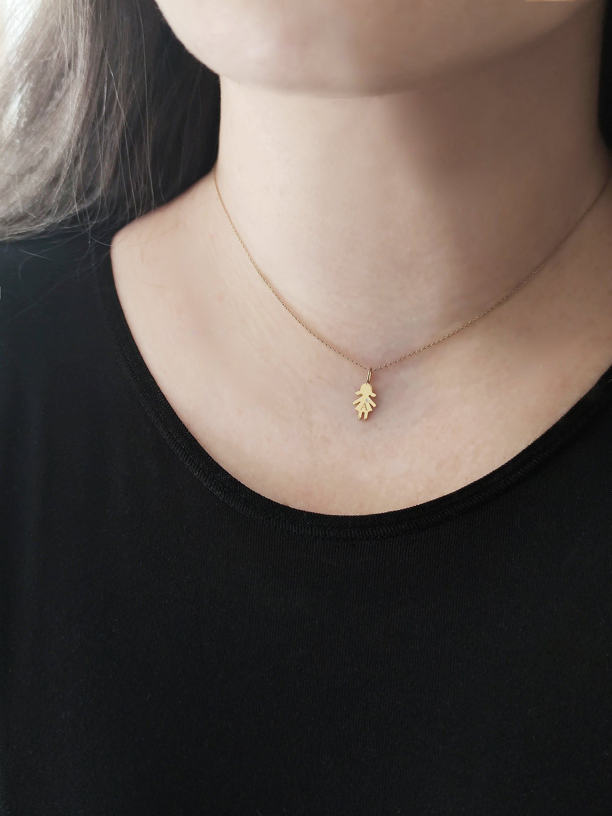 close up of a woman's neck wearing a gold necklace with a tiny girl charm engraved with a monogram and set with a tiny diamond