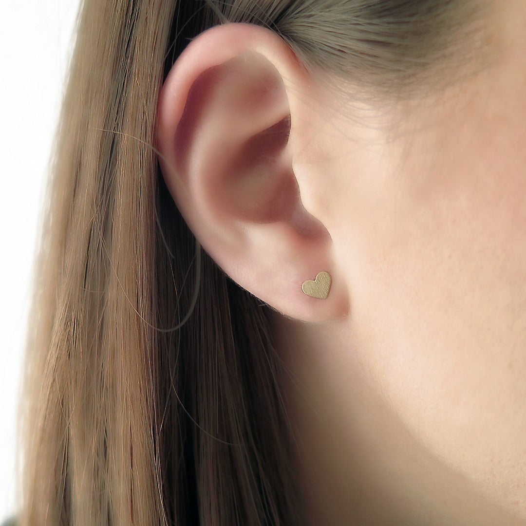 Woman wearing tiny solid gold heart-shaped stud earrings with matte finish