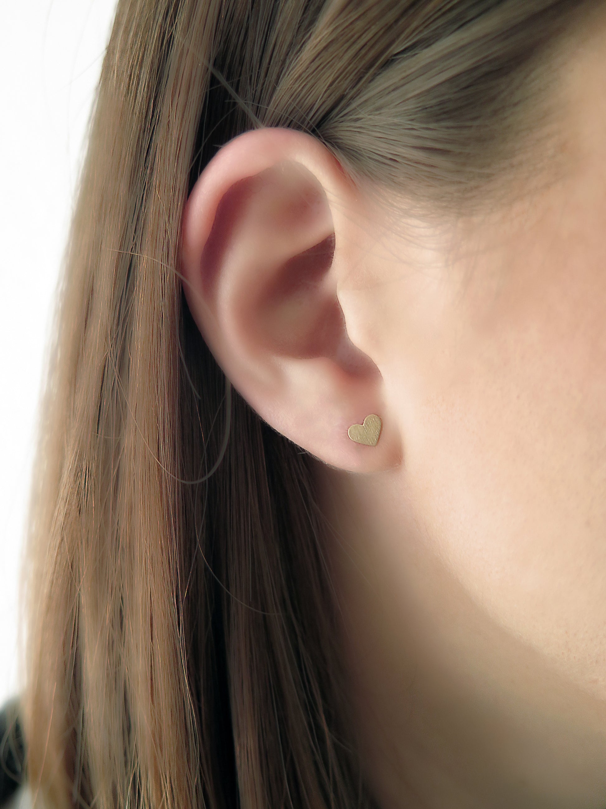 woman wearing tiny solid gold heart-shaped stud earrings with matte finish