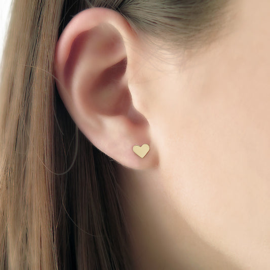 Close-up of an ear wearing a small gold heart-shaped stud earring.