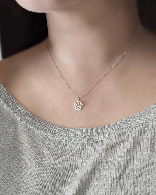 Woman wearing solid gold necklace with a tiny dog paw print pendant with a heart in the center
