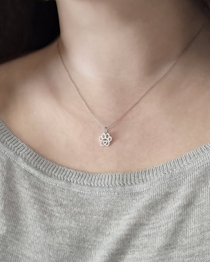 Necklace with a paw print pendant worn by a person in a gray top.
