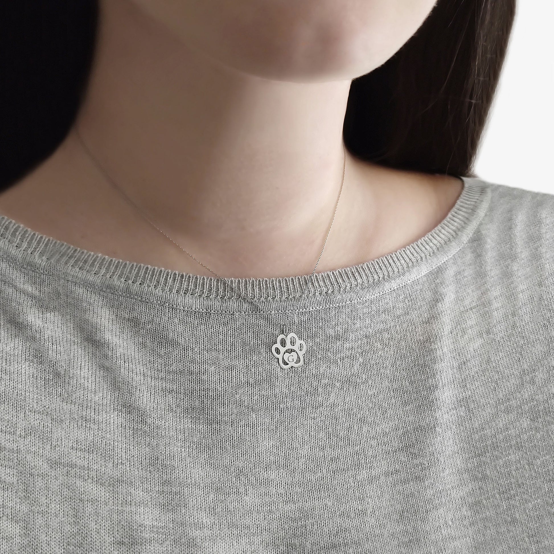 Close-up of a person wearing a gray sweater with a small paw print necklace .