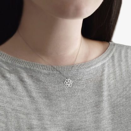 Close-up of a person wearing a gray sweater with a small paw print necklace .
